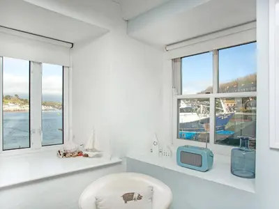 a white room with a tv and a chair and windows at The Lookout in Polruan