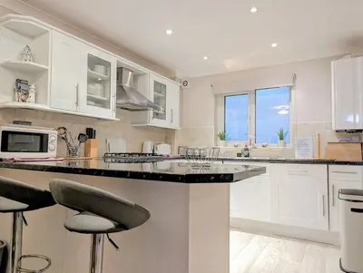 a kitchen with white cabinets and a counter with stools at Fistral beachside escape - dramatic ocean views in Crantock