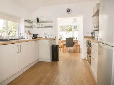 a kitchen with white cabinets and a wooden floor at Blacksmiths Cottage in Newquay