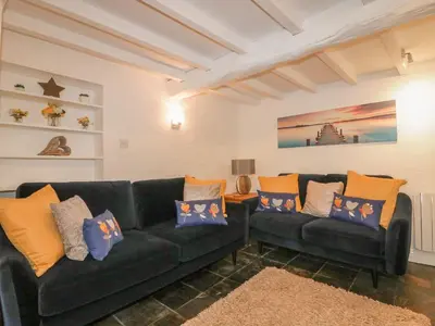 a living room with two black couches and a rug at Blacksmiths Cottage in Newquay