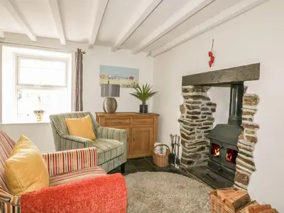 a living room with a stone fireplace with two chairs at Blacksmiths Cottage in Newquay