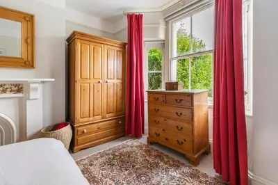 a bedroom with red curtains and a dresser and a window at La Folie, Fowey in Fowey