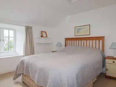 a white bedroom with a bed and a window at Trewillig Cottage in Wadebridge