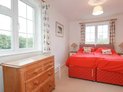 a bedroom with a red bed and two windows at Trewillig Cottage in Wadebridge