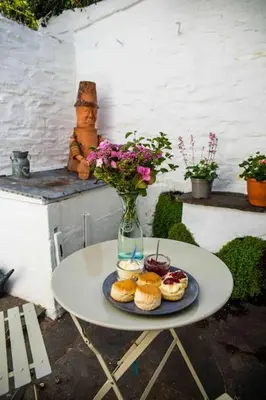 a table with a vase of flowers and pastries on it at Boscastle Quaint Cornish Fishermans Cottage in Boscastle