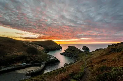 a sunset over a body of water with rocks at Boscastle Quaint Cornish Fishermans Cottage in Boscastle