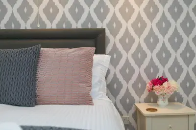 a bed with a pillow and a vase with flowers on a table at Ocean Edge in St Ives