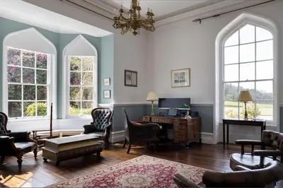 a living room with chairs and a desk and windows at Catchfrench Manor in Sheviock