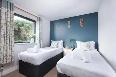 two beds in a room with blue walls and a window at Beachside in Newquay