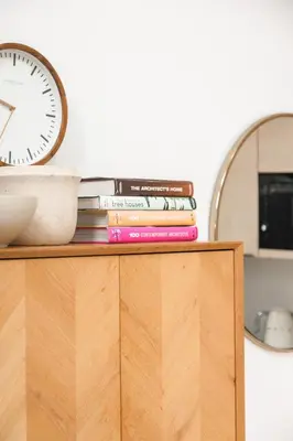 a stack of books on top of a dresser with a clock at Lowen Tree House in Truro