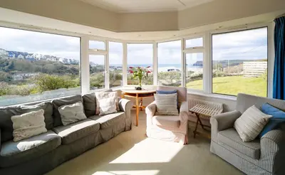 a living room with a couch and chairs and windows at Trevarthian in Polzeath
