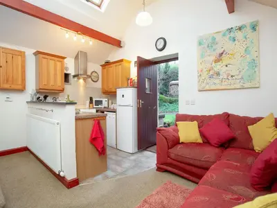a living room with a red couch and a kitchen at Bulls Cottage in Bodmin