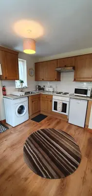a kitchen with white appliances and a wooden floor at 11 Granite Henge in Pelynt