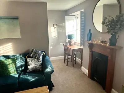 a living room with a black leather couch and a table at Ebb Tide - Fisherman's Cottage in Gorran Haven