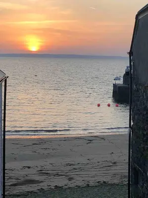 a sunset on the beach with the ocean and a building at Ebb Tide - Fisherman's Cottage in Gorran Haven