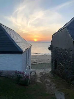 a building on the beach with the sunset in the background at Ebb Tide - Fisherman's Cottage in Gorran Haven