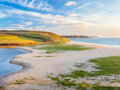 a sandy beach with the ocean and cliffs in the background at 4 Bed in Helston oc-90391 in Crowan