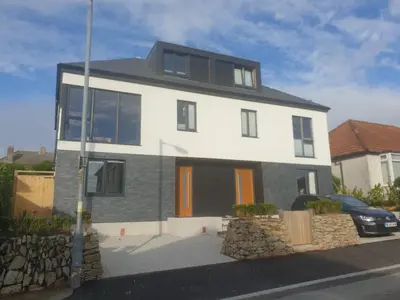 a white house with a car parked in front of it at Modern open plan house, sea views and hot tub in Falmouth