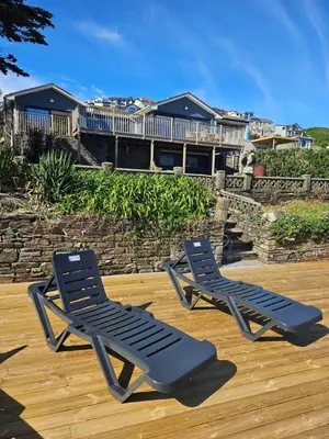 two lounge chairs on a deck with a house in the background at Stunning Front Line Ocean Views Luxury Beach House in Downderry