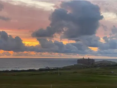 a building on a hill near the ocean at sunset at Bredon Court overlooking Fistral beach, Newquay in Newquay