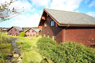 a large wooden house with a pathway leading to it at Holiday lodge, on-site watersports, Retallack Resort in Saint Columb Major