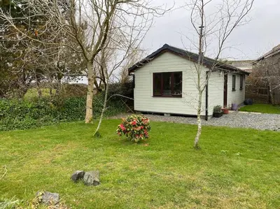 a white house in a yard with a tree and flowers at Idyllic Cornish Retreat At Puffin Lodge in Helston