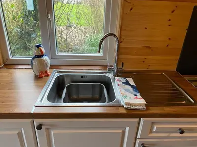 a kitchen sink with a bird sitting next to a window at Idyllic Cornish Retreat At Puffin Lodge in Helston