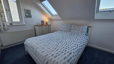 a bedroom with a bed and a dresser and windows at Driftwood in Porthtowan
