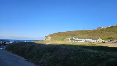 a view of a hill with a house and the ocean at Driftwood in Porthtowan