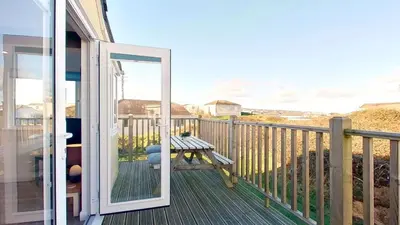 a sliding glass door leading to a deck with a table at F08 Carne Michael, Riviere Towans in Hayle
