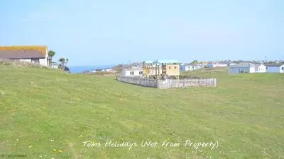 a grassy hill with houses and the ocean in the background at F08 Carne Michael, Riviere Towans in Hayle