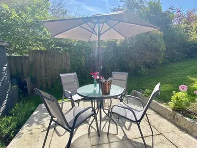 a table with chairs and an umbrella on a patio at About Time Meva - stylish two-bedroom, dog-friendly home-from-home with parking and garden in Mevagissey