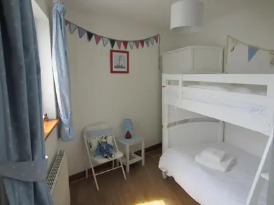 a bedroom with two bunk beds and a chair at Singing Cottage in Port Isaac
