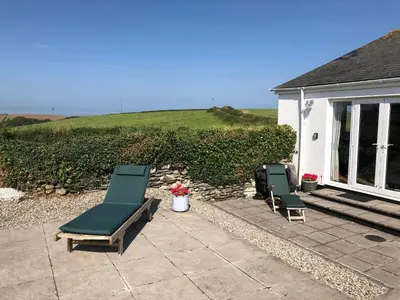 two lounge chairs and a patio with a house at Singing Cottage in Port Isaac
