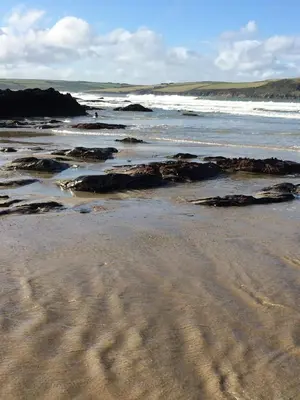 a sandy beach with rocks and the ocean at Singing Cottage in Port Isaac