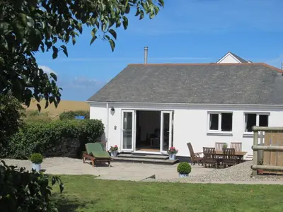 a white house with chairs and a patio at Singing Cottage in Port Isaac