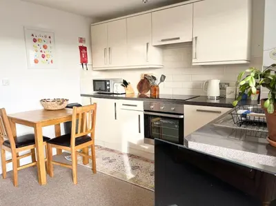 a kitchen with white cabinets and a wooden table and chairs at Seascape Stay No 4, Sea View & Parking in Falmouth
