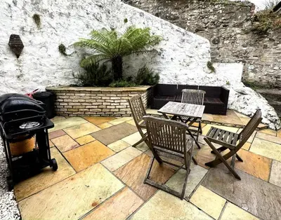 a patio with two chairs and a table and a grill at Charming Cornish Cottage in the heart of St Agnes in St. Agnes