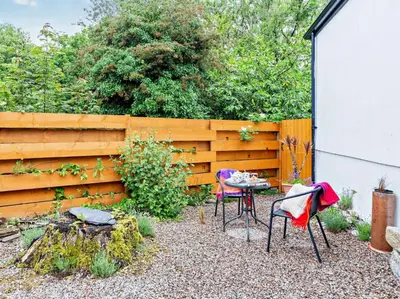 a garden with two chairs and a table in front of a fence at Tiptoe Barn in Liskeard