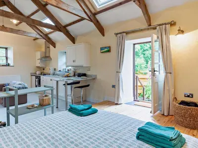 a room with a bed and a kitchen with a table at Tiptoe Barn in Liskeard