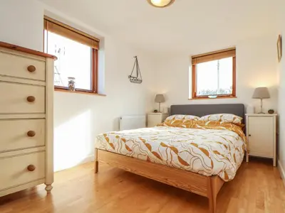 a bedroom with a bed and a dresser and two windows at Little Fernleigh in Helston