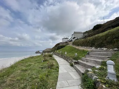 a path next to the ocean with a house on a hill at UPPER BEACH HOUSE in Portreath