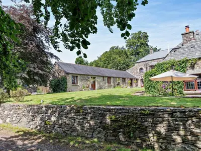 an exterior view of a stone house with an umbrella at 2 Bed in Callington oc-tyler in North Hill