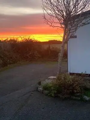 a building with a tree and a sunset in the background at Praa Sands - Apartment - Sleeps 2 - Parking in Praa Sands