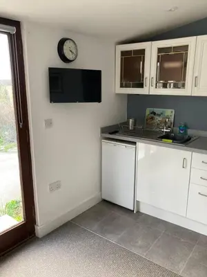 a kitchen with white cabinets and a clock on the wall at Praa Sands - Apartment - Sleeps 2 - Parking in Praa Sands
