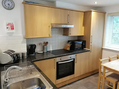 a kitchen with wooden cabinets and a sink and a microwave at Cornwall Holiday Home, Casa Da Praia in Saint Columb Major