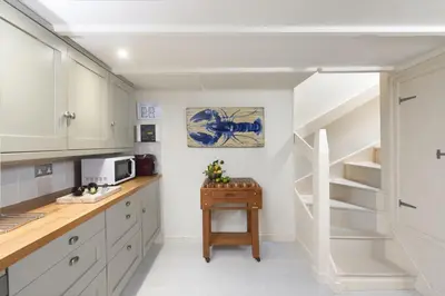 a kitchen with white cabinets and a spiral staircase at Tathra Beach Cottage in St Ives