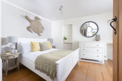 a white bedroom with a bed and a mirror at Tathra Beach Cottage in St Ives
