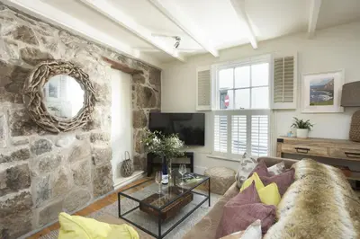 a living room with a couch and a stone wall at Tathra Beach Cottage in St Ives