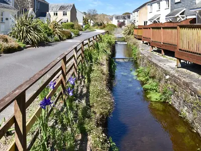 a river next to a bridge with blue flowers at Chy Morvoren in Falmouth